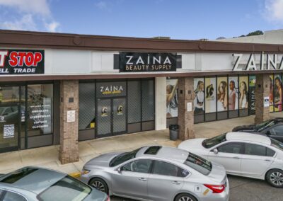 A row of busy businesses, including Zaina Beauty Supply, with multiple cars out front at the Akers Center in Gastonia NC