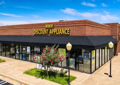 Storefront for the corner unit Locke Discount Appliance at Heritage Plaza in Midwest City OK with lovely pink flowering bushes out front